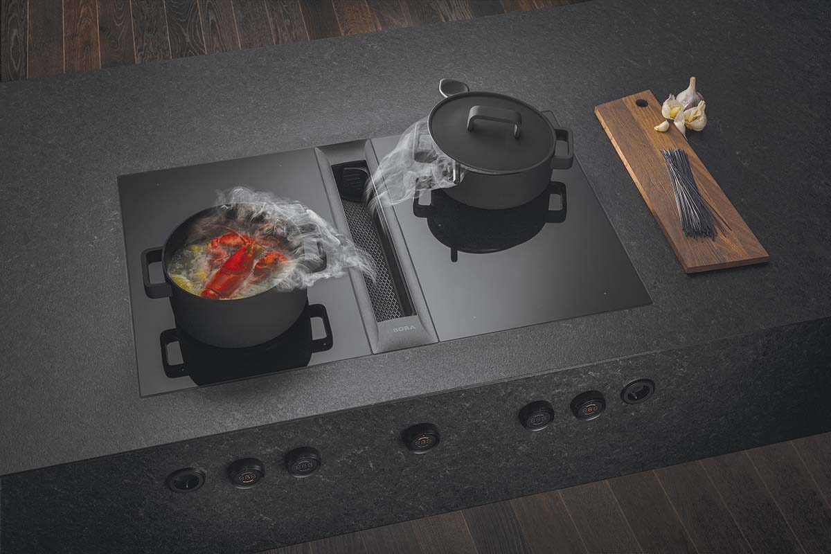 a black hob with two pans steaming on it with vegetables in them
