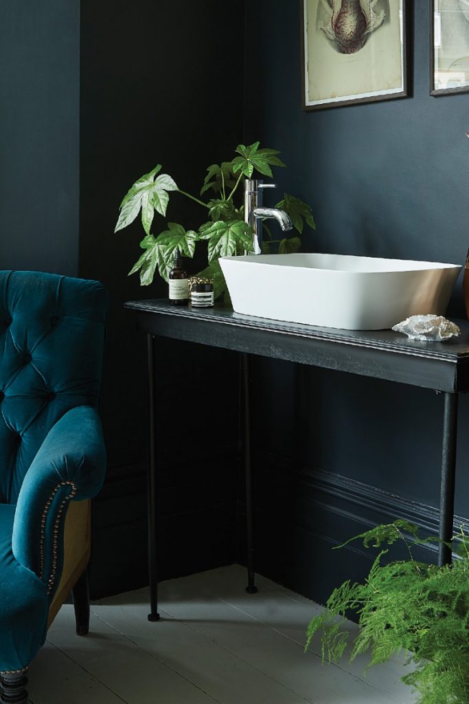 a bedroom with a dark interior, a teal armchair and a white basin on top of a black stand