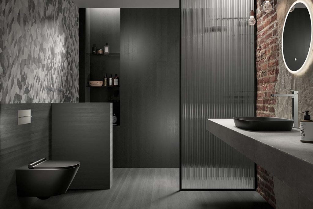 a dark and bold shower enclosure with a fluted glass panel, black sanitaryware and exposed brickwork