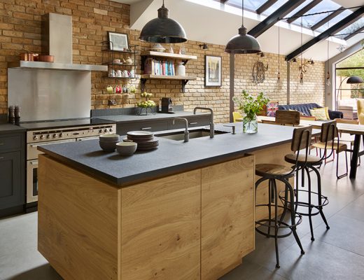 a modern rustic kitchen featuring a dark grey island with wooden cabinetry and three charcoal pendant lights above it, illustrating how to make your kitchen bigger