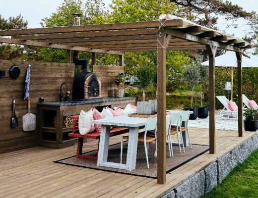 an outdoor kitchen design featuring a wooden gazebo and white table and chairs on oak decking
