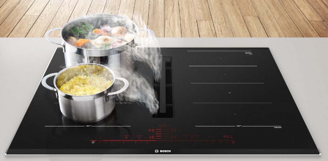 a hob with extractor in a kitchen with two stainless steel pans containing food steaming on top of it