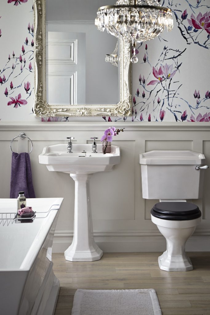 a traditional bathroom with floral wallpaper, a chandelier, a gilt mirror and a traditional pedestal basin and toilet