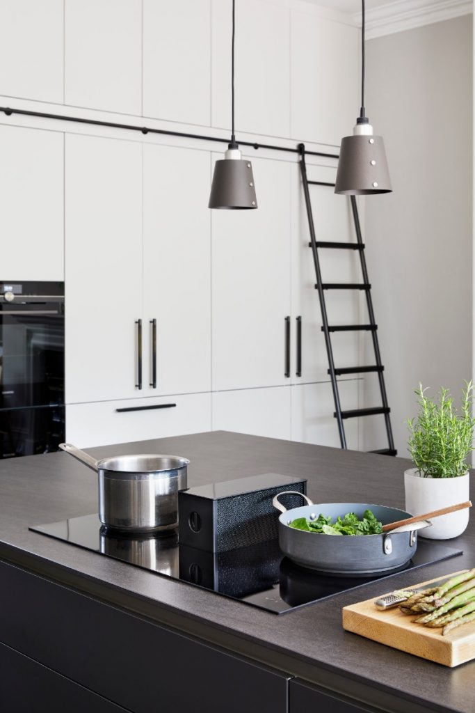 a hob with extractor in a kitchen with two stainless steel pans containing food on top of it. There is a ladder leaning against wall cupboards in the background