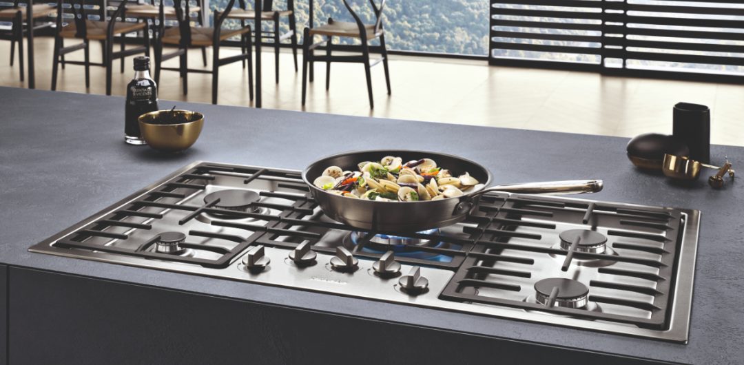 Miele black gas hobs with a pan full of vegetables on a burner