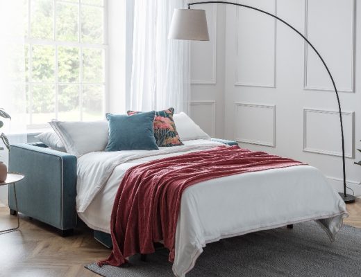 a double sofa bed with teal and floral cushions and an arc floor lamp with a grey shade