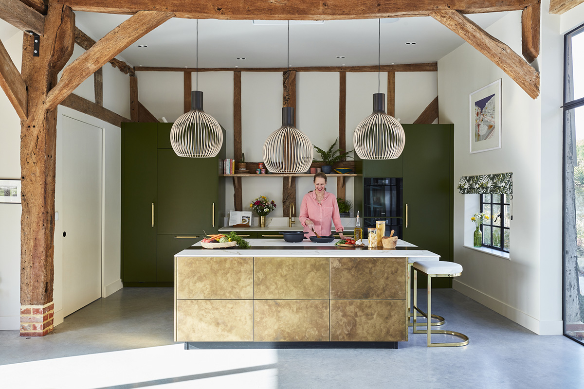 a sola kitchens design featuring a woman standing at a beige and white kitchen island preparing food, while three pendant lights hang above her 