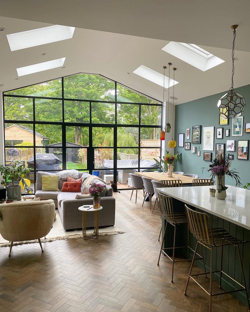 a spacious living area with a sofa, dining table and chairs and black steel framed glazing behind it