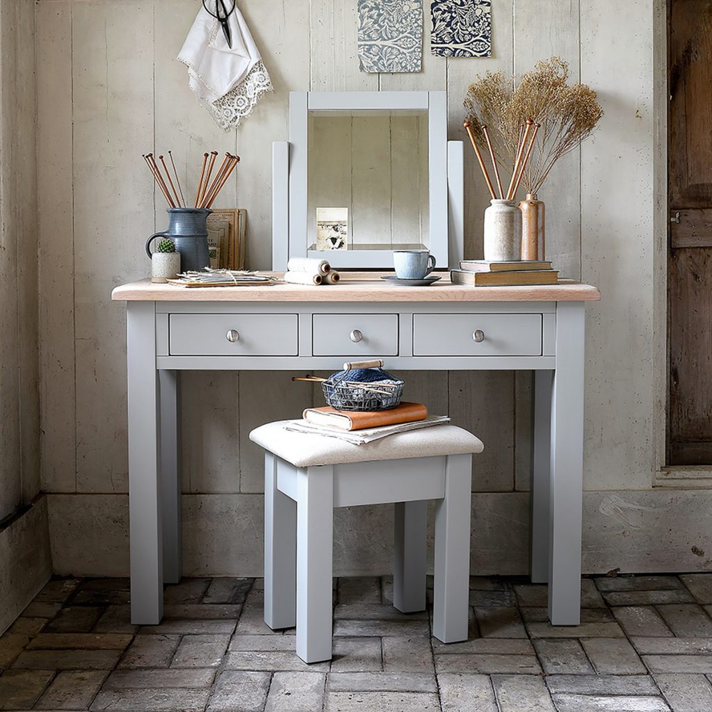 a grey dressing room table with three silver knobs and a wooden top with accessories and a mirror on top
