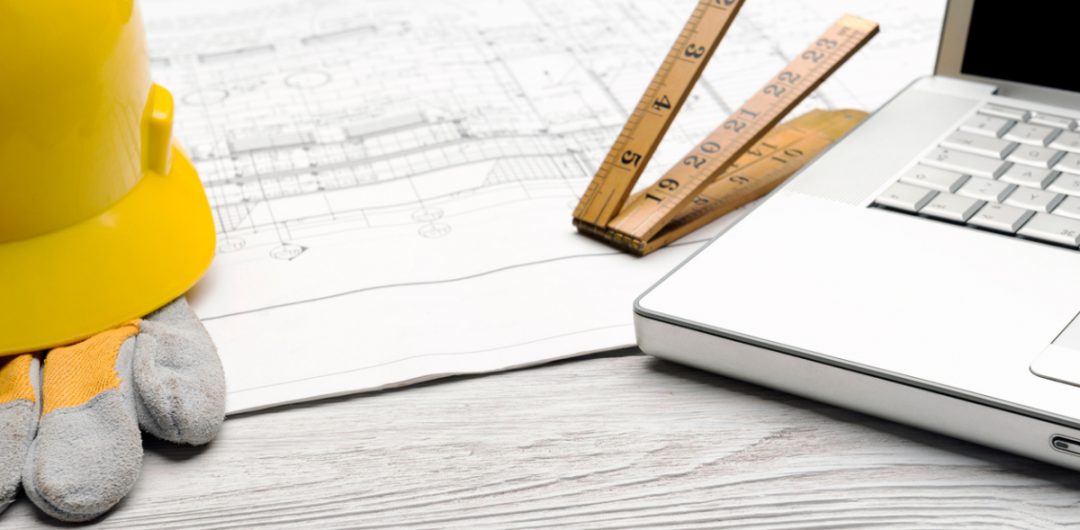 a silver laptop next to a wooden tape measure and architect's plans