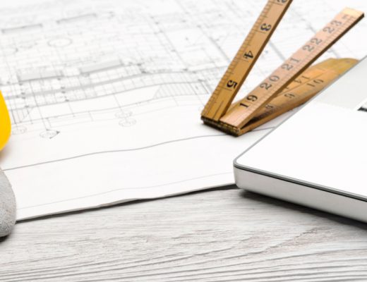 a silver laptop next to a wooden tape measure and architect's plans