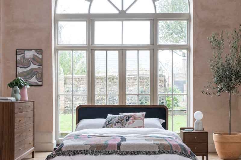 Calming bedroom design with wood furniture, big bed in front of a bright window, a cosy rug and house plants